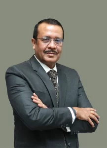 Rabi Dasgupta, Co-Founder and Managing Director of Acumen Global, in formal attire, standing confidently with folded arms.